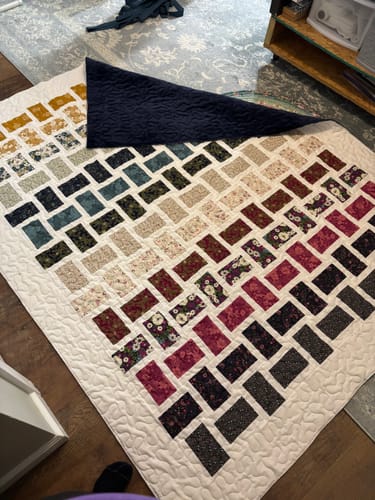 Customer's completed Dream Weaving quilt featuring a gradient of Chelsea Garden fabrics and a dark blue backing.