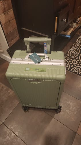 Customer's green NOBL suitcase standing upright on tiled flooring