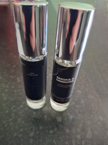 Customer's two glass fragrance bottles with silver caps standing on a dark surface, including Mr Carter.