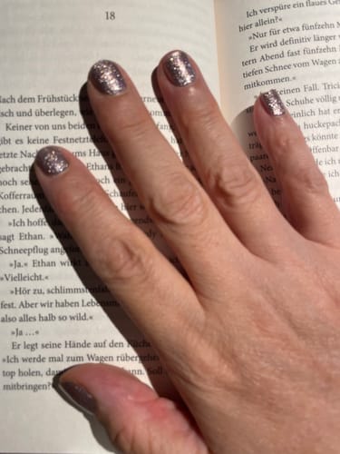 Reviewer's hand showing UV Gel Elegant Glow nail wraps in a rosy glitter finish, while holding an open book.