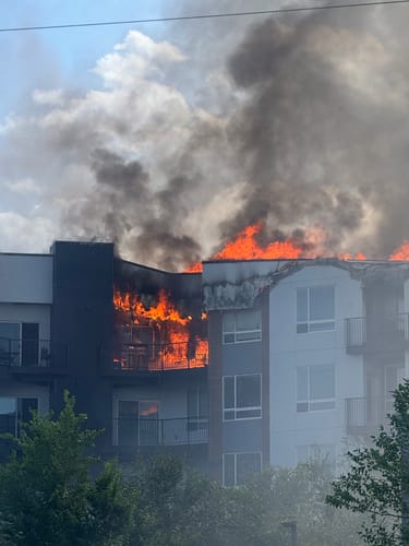 Reviewer's photograph of a residential apartment building engulfed in flames and smoke from a fire.
