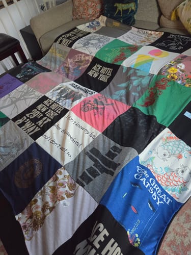 Customer's custom Project Repat T-Shirt Quilt featuring various colorful graphic t-shirt panels spread on a sofa.