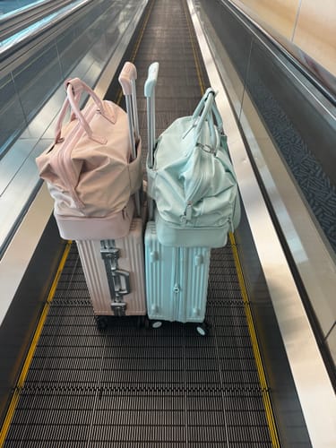 Customer's pink and light blue NOBL suitcases with matching carry-on bags on an airport moving walkway.