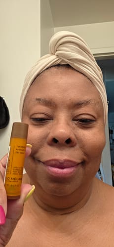 Reviewer holding a Glo Melanin lip balm tube in their hand with a head wrap on.