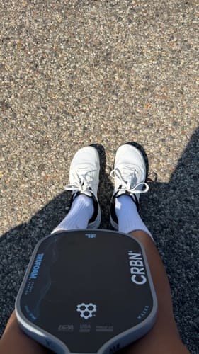 Customer's white CUURT Muuv court shoes being worn with a pickleball paddle resting on their lap.