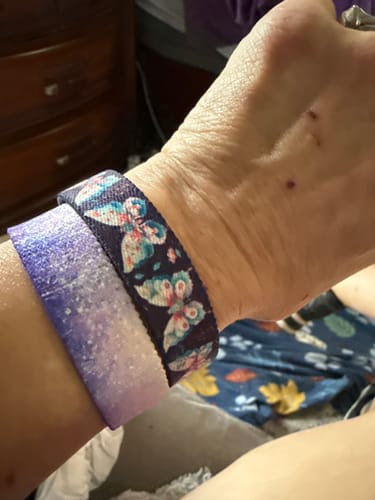 Customer's wrist wearing two patterned bracelets, one with butterfly designs, the other with a purple gradient.