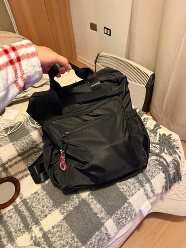 Customer's black nylon Mochila Icónica held by hand, showing front pockets and a colorful keychain.