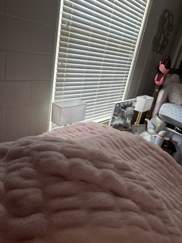 Customer's soft pale pink Hugs Light Carnation blanket draped over a bed near a window