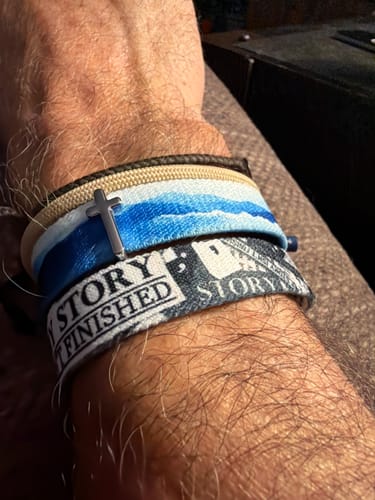 Reviewer's wrist wearing a blue and white God Is In Control Bible Verse Bracelet featuring a silver cross charm.