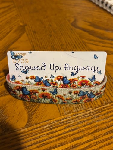 Reviewer's Showed Up Anyway bracelet with floral and butterfly pattern, resting on an information card.