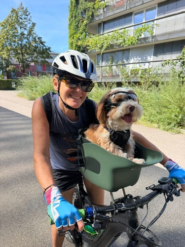 Reviewer's green Kvisp Dog Bike Carrier on a bike, featuring a happy small dog wearing goggles.