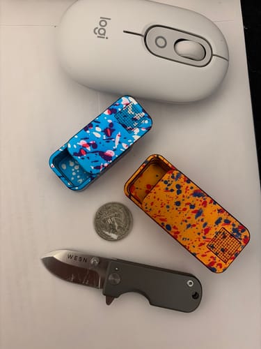 Customer's two Nano Case pill containers with colorful paint splatters, sitting next to a computer mouse and small knife.