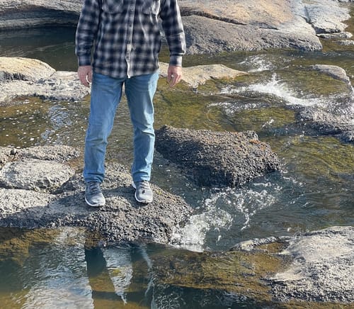 Reviewer's Women's Xdrain Crew shoes worn on feet while standing on wet rocks in a shallow stream.