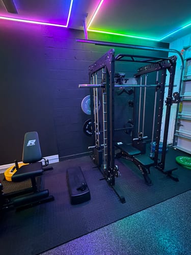 Customer's RitFit WSM1 Weight Stack set installed on a black M1 Smith machine in a home gym with colorful lighting.