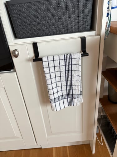 Customer's sort håndkleholder i metall montert over en lys kjøkkenskapdør med et rutete håndkle hengende.