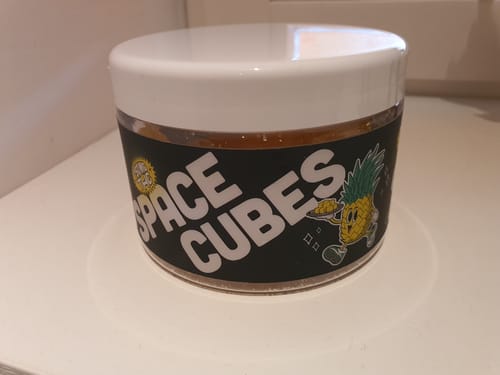 Kundenfoto der runden THC Space Cubes Dose mit Ananas-Motiv auf einer weißen Oberfläche.
