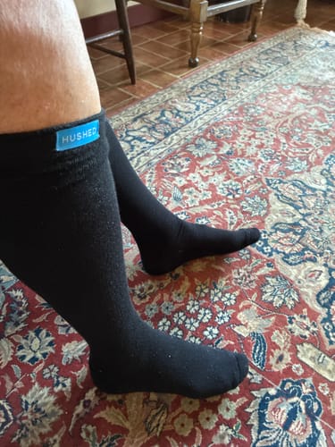 Customer's black Hushed compression socks worn on feet, featuring a blue brand label, over a patterned rug.