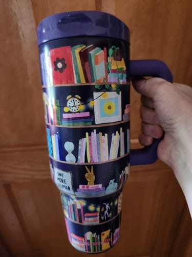 Customer's purple Thicc Buddy 40oz mug with colorful bookshelf pattern, held in a hand.