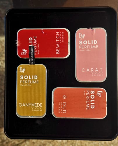 Customer's set of four solid perfume tins, including Ganymede, G Oud, Carat, and Bewitch, arranged in a dark case.