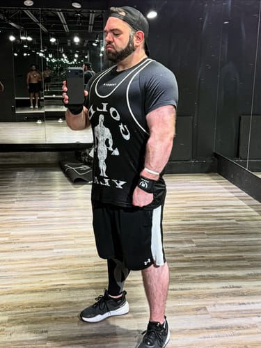 Reviewer wearing a black Golds Gym Classic Stringer in a gym mirror selfie.