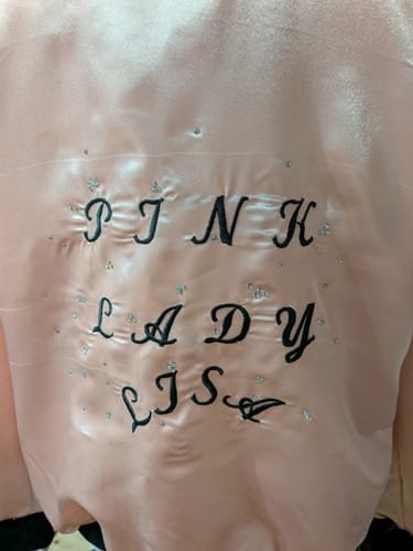 Customer's pink liquid satin fabric embroidered with black lettering and scattered rhinestones.