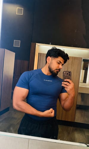 Customer's blue 475 SuperVillain Compression Tee on a person flexing in a gym mirror.
