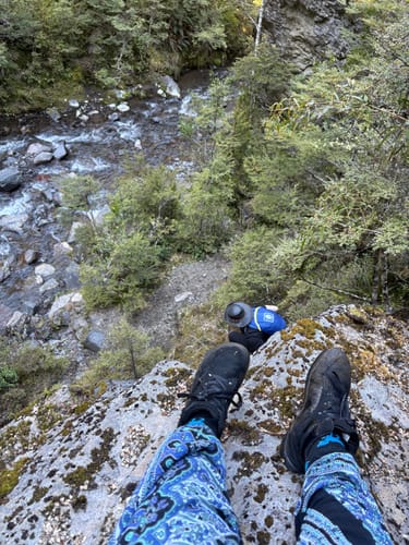 Reviewer's black Wonderland Lite barefoot shoes while perched on a rocky cliff overlooking a river.