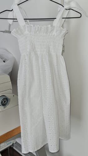 Customer's white eyelet muslin dress hanging on a hanger near a sewing machine.