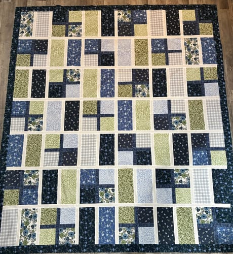 Customer's Apple Cider Quilt Kit laid out on a floor, featuring navy and green floral blocks with a custom border.