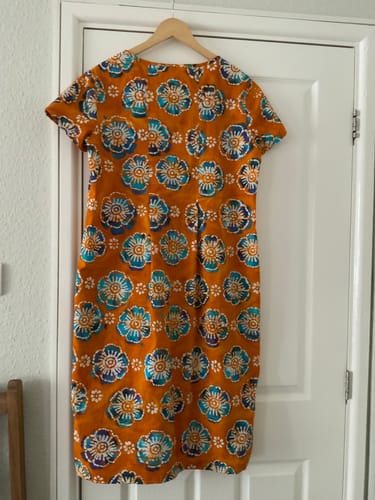 Customer's Milenda dress made from the orange Bloom Circle cotton batik fabric, hanging on a door.