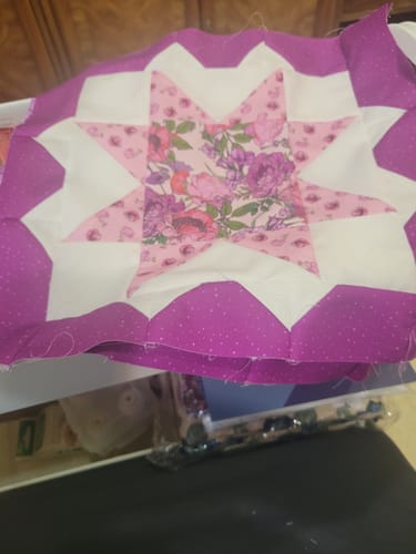 Reviewer's sewn floral star quilt block from the Granny Squares kit, featuring pink fabric with purple floral accents.