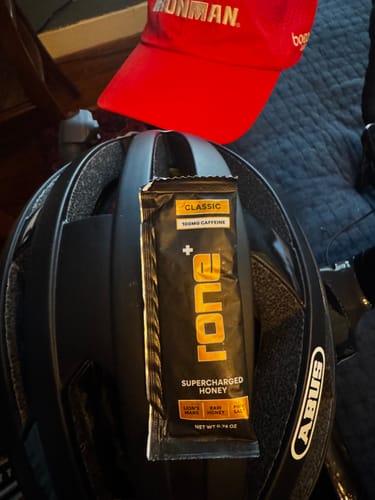 Customer's 100mg Caffeine SuperCharged Honey packet resting on a black bike helmet near a red hat