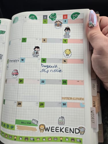 Reviewer's hand holding an Ultimate Subscription planner filled with creative stickers and colorful washi tape.