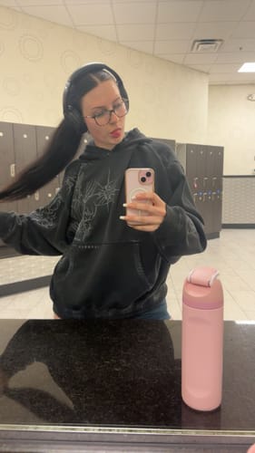 Reviewer's oversized, washed-black Cyberpunk Hoodie with graphic linework, shown in a mirror selfie at a gym.