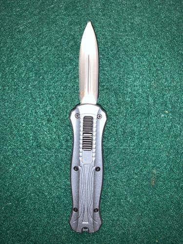 Customer's VT Black Rocket Mini OTF knife with metallic handle and deployed stainless steel blade on green surface.