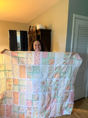 Reviewer holding a large, handmade patchwork quilt with soft pastel floral and geometric patterns.