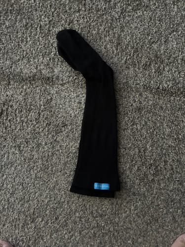 Customer's black Eucalyptus Lyocell Compression Sock laying flat on a textured carpet.