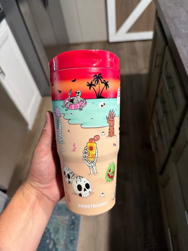 Reviewer's To-Go Buddy cup featuring a colorful beach-themed design with skeletons and a pink lid, held in hand.