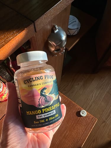 Customer's hand holding a bottle of Cycling Frog Mango Pineapple gummies.