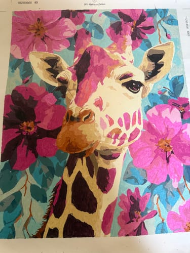 Kundenfoto des fertiggestellten Malen nach Zahlen Sets Lila Giraffe, das eine Giraffe vor blauen Blumen zeigt.