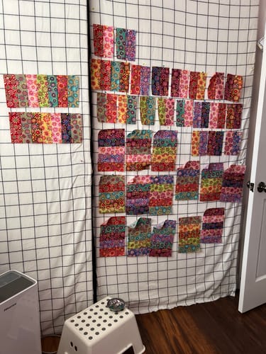 Customer's Crazy Daisy Pre-Cut Quilt Kit with fabric pieces pinned to a grid wall for layout.