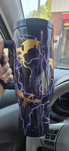 Customer's dark purple Thicc Buddy 40oz mug with gold dragon silhouettes and lightning patterns held inside a car.