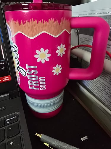 Customer's pink Thicc Buddy 16oz cup with daisy patterns, resting on a desk next to a laptop.