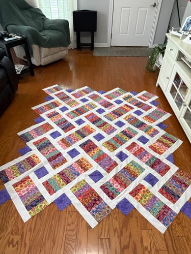 Customer's Crazy Daisy Pre-Cut Quilt Kit fully assembled in a vibrant, patterned throw size on a wooden floor.