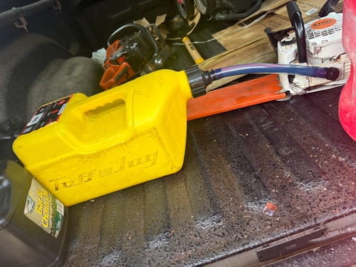 Customer's yellow TuffJug fuel can resting horizontally in a truck bed, connected to a white chainsaw.