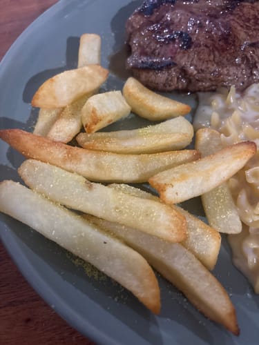 Customer's Chooki's Original Chicken Salt sprinkled over hot chips served on a plate with a steak dinner.