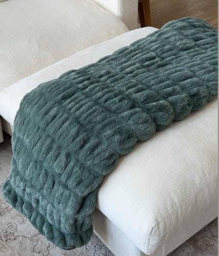 Customer's forest green Hugs Alpine Blanket draped over a white couch.
