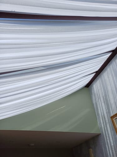Customer's white muslin fabric draped elegantly as swags across a glass roof to block sunlight.