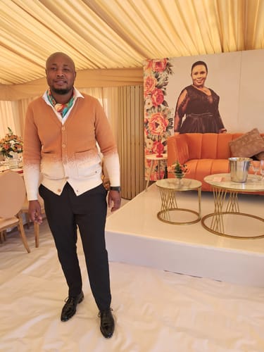 Reviewer's Camel LFN045 cardigan worn with a scarf and black trousers in a decorated indoor venue.