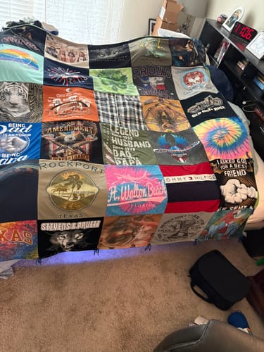 Customer's Project Repat T-Shirt Quilt displayed on a bed, showing a patchwork of colorful, patterned t-shirt squares.
